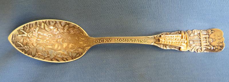 Souvenir Mining Spoon Leadville.JPG - SOUVENIR MINING SPOON LEADVILLE CO - Sterling silver spoon, 5 3/4 in. long, embossed mining scene of miners working underground in bowl, handle marked ROCKY MOUNTAINS showing a winch lowering a bucket into bowl, special decoration on handle of gold mining tools sledge, pick and shovel, reverse marked with maker’s mark, COLORADO SILVER and engraved LEADVILLE, ca.1910, weight 27.5 gms. [Leadville CO is the highest incorporated city in the United States. A former silver mining town that lies near the headwaters of the Arkansas River in the heart of the Rocky Mountains, the city includes the Leadville Historic District, which preserves many historic structures and sites from Leadville's dynamic mining era. Gold was discovered in the area in late 1859, during the Pike's Peak Gold Rush. However the initial discovery, where California Gulch empties into the Arkansas River, was not rich enough to cause excitement. On April 26, 1860, Abe Lee made a rich discovery of placer gold in California Gulch, about a mile east of Leadville, and Oro City was founded at the new diggings.  By July 1860, the town and surrounding area had a population of 10,000 and an estimated $2 million in gold was taken out of California Gulch and nearby Iowa Gulch by the end of the first summer. Within a few years the richest part of the placers had been exhausted, and the population of Oro City dwindled to only several hundred.   However, in 1874 gold miners at Oro City discovered that the heavy sand that impeded their gold recovery was the lead mineral cerussite that carried a high content of silver. Prospectors traced the cerussite to its source, and by 1876, had discovered several lode silver-lead deposits. A number of silver mines were established on Iron Hill and Carbonate Hill, east of town.  The city of Leadville was founded near the new silver deposits in 1877 by mine owners Horace Austin Warner Tabor and August Meyer, setting off the Colorado Silver Boom. By 1880, Leadville was one of the world's largest silver camps, with a population of over 40,000. The city's fortunes declined with the repeal of the Sherman Silver Purchase Act in 1893 which resulted in a drop in the price of silver.]  